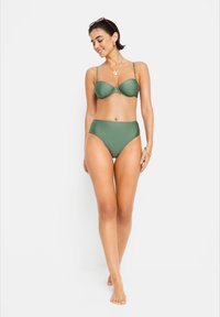 Žalias bikini komplektas su paminkštintu liemenėliu, reguliuojamomis petnešomis ir aukštu juosmeniu. Lygus paviršius, minimalistinis dizainas ir tinkamumas lauko veiklai.