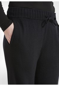 Zwarte gebreide joggers met een geribde tailleband met trekkoord en zijzakken, die een zachte, gestructureerde afwerking tonen.