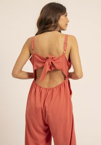 Combinaison en corail avec bretelles spaghetti, dos nu et détail de nœud. Tissu doux et lisse avec une coupe ample et décontractée. Taille élastique.