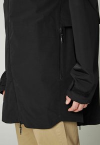 Čierna nepremokavá bunda s aerodynamickým dizajnom, vybavená bočnou kapsou, nastaviteľnými manžetami na suchý zips a elegantným matným povrchom.