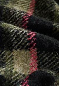 Tessuto di lana con motivo pied de poule in verde scuro, nero e rosa, con un aspetto morbido e strutturato e spessore del filo variabile.