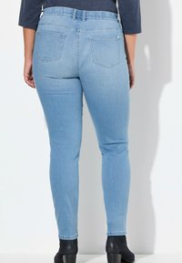 Jeans ajustados de mezclilla elásticos en azul claro con una cintura alta, cuatro bolsillos y una textura suave, combinados con botines negros.