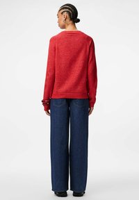 Raudonas tekstūruotas megztinis su ilgomis rankovėmis, raukšlėtais rankogalviais ir apvaliu kaklu, derinamas su aukštu liemeniu plačiomis mėlynomis džinsomis.