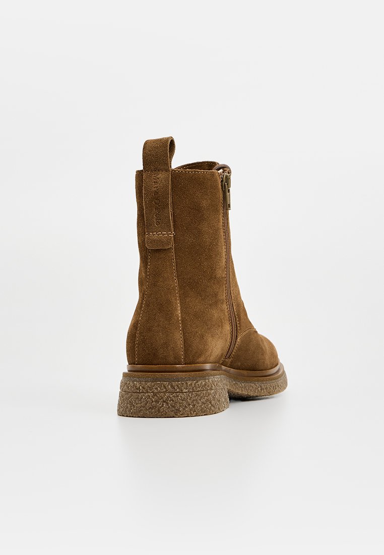 Braune Wildleder-Stiefelette mit seitlichem Reißverschluss, Zugschlaufe und strukturiertem Gummisohle auf weißem Hintergrund, von hinten rechts betrachtet.