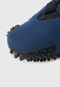 Μπλε αθλητικό παπούτσι με διάτρητο υλικό και μαύρη ελαστική σόλα με έντονες ακίδες για πρόσφυση και ενισχυμένη περιοχή στα δάχτυλα.