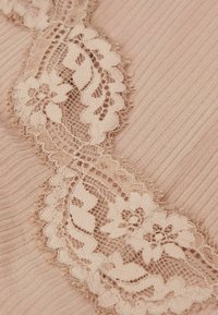 Beige stof met verticale ribbels, voorzien van bloemenkant trim in een lichte toon, zachte textuur en delicate geprofileerde randen.