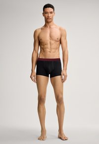 Černé boxerky mají vínový elastický pás. Jsou vyrobeny z měkké, pružné tkaniny. Design nabízí přiléhavý siluetu.