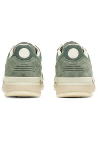 Green suede athletic shoes with beige rubber soles, featuring a round white accent at the heel and textured details on the upper back.