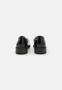 Black patent leather shoes with a smooth finish, rounded toe, and low black heel, featuring minimal stitching and no visible hardware.