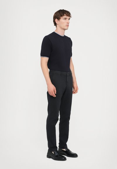 Chemise à manches courtes marine avec col bleu clair contrastant, assortie à un pantalon noir slim-fit et des mocassins noirs. Design minimaliste, forme ajustée.