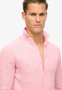 Camisa a rayas rojas y blancas, diseño de botones con cuello alzado y botones visibles, fabricada en tejido ligero con un acabado texturizado.