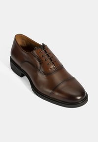 Bruine leren dresschoenen met een ronde neus, voorzien van een vetersluiting en een getextureerde rubbere zool voor extra grip.