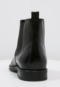 Czarny skórzany botek Chelsea z elastycznymi panelami bocznymi, zaokrąglonym noskiem i płaską, drewnianą podeszwą. Gładka faktura z minimalistycznym wzorem.