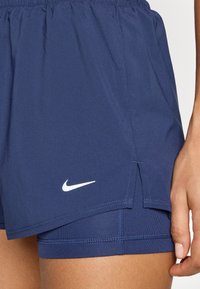 Navy athletic shorts with built-in shorts underneath, featuring a small white Nike logo, elastic waistband, and side slits for mobility.