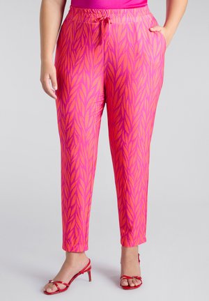 Pantalon rose à motif de feuilles, avec taille élastique, poches latérales et jambes fuselées, associé à des talons rouges à brides.