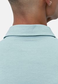 Lyseblå polo skjorte med en myk tekstur, med en standard krage og synlig søm ved nakken. Bakview viser glatt stoff.