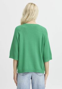 Grüner Pullover mit kurzen Ärmeln, gerippten Bündchen und Saum. Hergestellt aus weichem Strickstoff, mit entspannter Passform und nahtlosen Schultern.