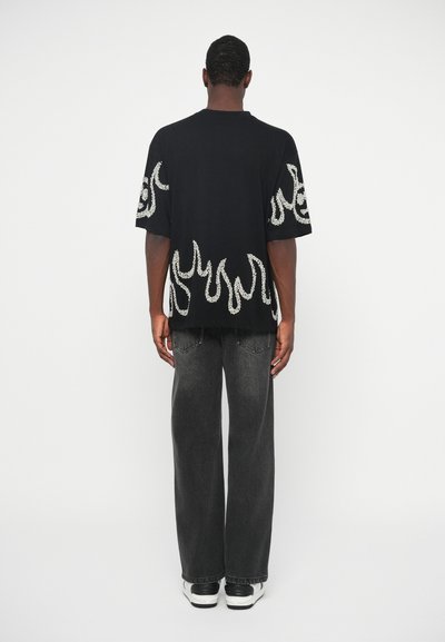 Musta suurte lühikeste varrukatega T-särk valgete leekmustriga; koos hallide vabalt istuvate teksade ja mustade-valgete spordijalatsitega.