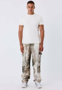 Witte T-shirt met korte mouwen, gecombineerd met losse cargobroek in camouflagepatroon met zakken en gedempte aardetinten, aangevuld met witte sneakers.