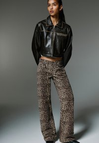 Veste en cuir noire courte avec fermeture à glissière et grand col, associée à un pantalon large à motifs léopard marron. Textures lisses partout.