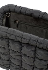 Mustat tikatut laukut, joissa on teksturoitu pinta ja sisällä zip-pussi. Pehmeä kangas, jossa on pyöreitä osia ja tasainen pohjamuoto.