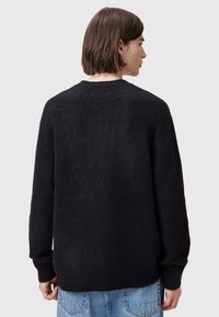 Svart strikket genser med avslappet passform, ribbede mansjetter og rund hals. Teksturert stoff synlig fra bakvinkelen. Kombinert med blå jeans.