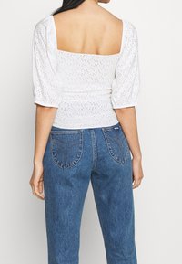 White short-sleeve top with a square neckline and perforated design paired with high-waisted blue denim jeans featuring back pocket detailing.