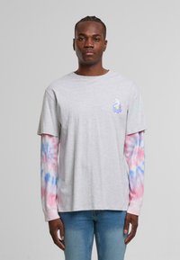 Grå t-skjorte med korte ermer lagdelt over lange tie-dye ermer i rosa og blå. Har et tegneserie-motiv på brystet.
