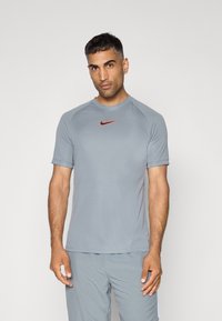 Hallideh erakordne lühikeste varrukatega hall sportlane särk, ümmarguse kaelusega ja väikese punase Nike logoga rinnal. Sile tekstuur, kerge kaal, ehkki vormistatud disain.