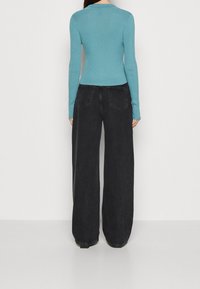 Maglione aderente turchese a coste con maniche lunghe abbinato a jeans neri a gamba larga con tasche posteriori e vita alta.