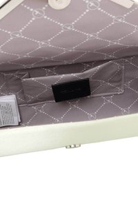 Vit handväska inuti med en slät textur, som har ett grått mönstrat foder och en liten svart ficka. Stängningsknapp synlig.