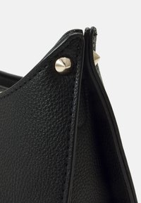 Sorte lædertaske med en tekstureret overflade, spids form og sølvhardware med en nitte detalje ved toppen.