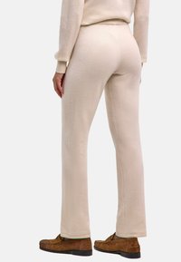 Beżowe dzianinowe spodnie o lekko prążkowanej fakturze, z prostymi nogawkami. Noszone z brązowymi zamszowymi butami, prezentującymi prosty, miękki wygląd.