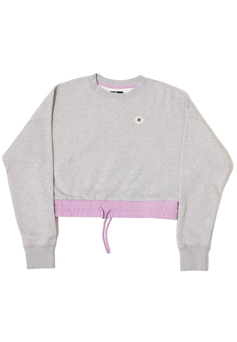 Sudadera corta gris con mangas largas, cinturilla elástica de color lavanda y un pequeño logo redondo cerca del escote. Material suave de mezcla de algodón.