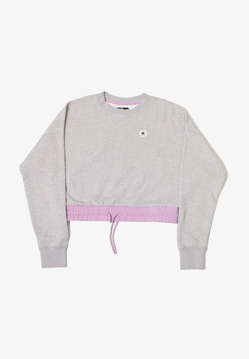 Sudadera corta gris con mangas largas, cinturilla elástica de color lavanda y un pequeño logo redondo cerca del escote. Material suave de mezcla de algodón.