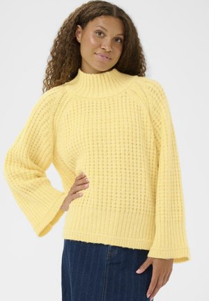 Gul strikket sweater med høj hals, lange klokkeærmer, struktureret ribstrik og en afslappet pasform, kombineret med et denimskørt.