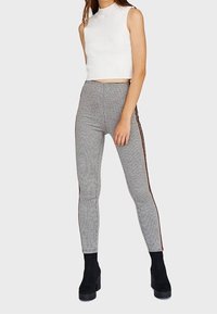 Leggings gris con rayas laterales, combinados con un top corto ajustado blanco y botas de tobillo negras con plataforma. Textura suave, ajuste a medida.