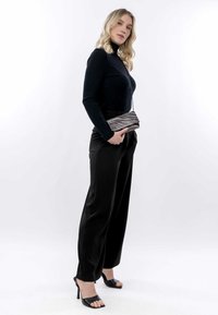 Must küllkihiline must särk, kõrge vöökohaga mustad püksid ja avatud varvastega mustad kontsad. Hoides sidurit, millel on hõbedane siksakmuster ja ketistrap.