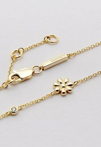 Goldfarbener Kettenarmreif mit einem floralen Anhänger und einem Kristallakzent, ausgestattet mit einem Karabinerverschluss und einem gravierten Etikett.