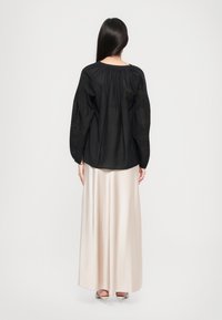 Sort langærmet bluse med draperede skuldre, parret med en flydende, lyse beige satin nederdel. Glat tekstur og klassisk silhuet.