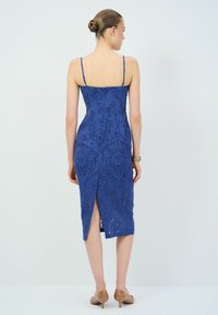 Robe en dentelle bleu royal avec des bretelles fines, silhouette ajustée, fermeture éclair au dos et une fente haute à l'ourlet. Motif lisse et texturé sur l'ensemble.