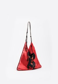 Czerwona satynowa torba w kształcie trójkąta z czarnym i brązowym wzorem psa, z pojedynczym paskiem i kontrastowym białym wykończeniem wzdłuż krawędzi.