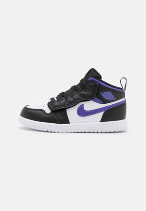 Basket Nike Air Jordan mid-top noire, blanche et violette avec swoosh et logo violet, lacets noirs et semelle blanche sur fond uni.