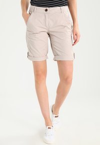 Shorts en coton beige avec ourlets retroussés, dotés d'un bouton unique à l'avant, de poches latérales et d'une coupe décontractée, associés à des baskets blanches.