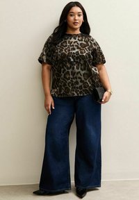 Leren top met luipaardprint, korte mouwen, gecombineerd met donkere blauwe wijde jeans. Een zwarte clutch en puntige zwarte schoenen maken de look compleet.