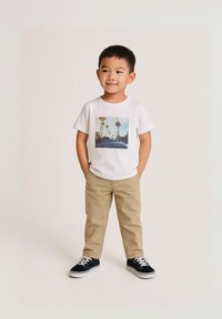 Weißes T-Shirt mit einem Palmenbaum-Design, khakifarbene Hose und schwarze Sneaker mit weißen Sohlen, im lässigen Schnitt und mit glatter Textur.