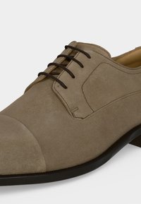 Chaussure habillée en daim marron clair pour homme avec lacets noirs et semelle noire, avec bout droit et coutures détaillées.