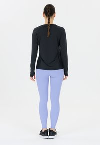 Svart långärmad atletisk topp i kombination med lavendel leggings. Toppens design har rund halsringning och sitter tajt; leggingsen är släta och elastiska.