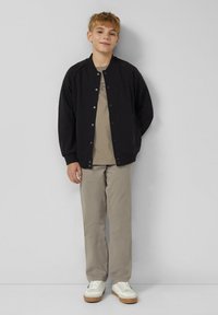 Czarna lekka kurtka bomberka z zatrzaskami, beżowy t-shirt pod spodem, jasnoszare spodnie i białe trampki z jasnobrązowymi podeszwami.