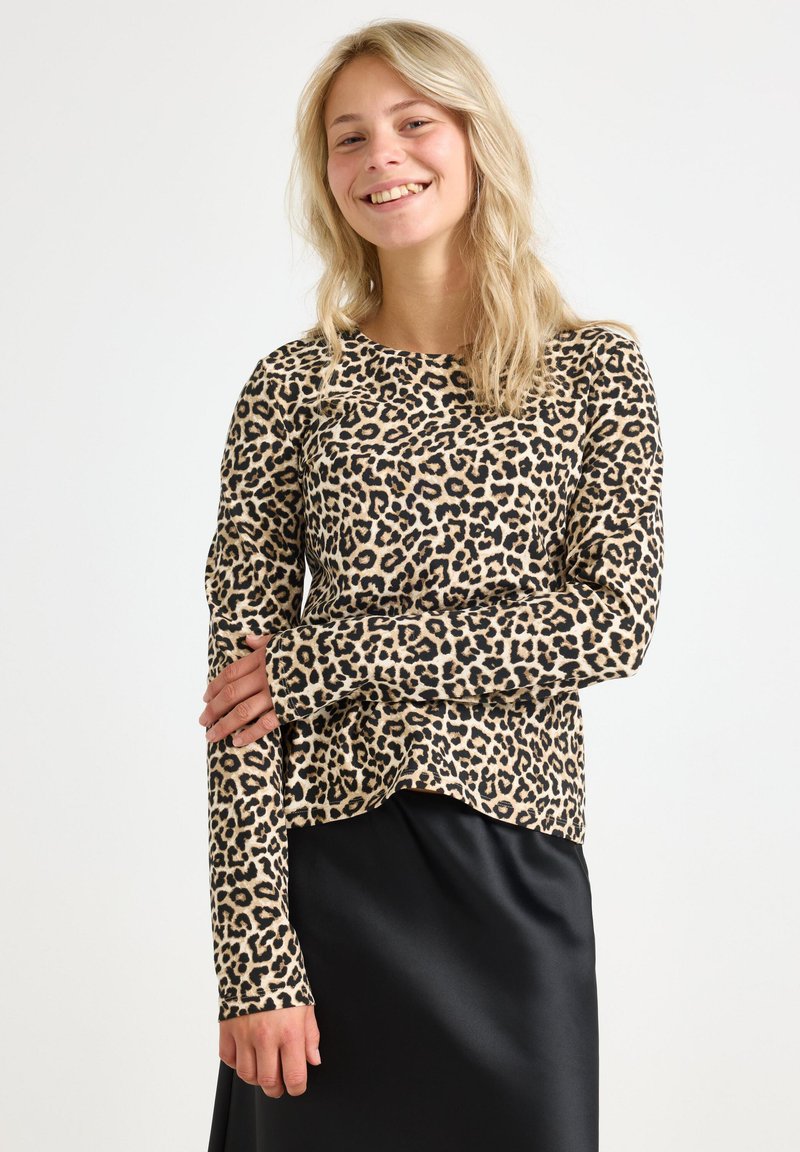 Leopardmönstrad långärmad topp i beige och svart, tillverkad av mjukt tyg, med rund halsringning och en lätt böjd fåll. Matchad med en svart satin kjol.
